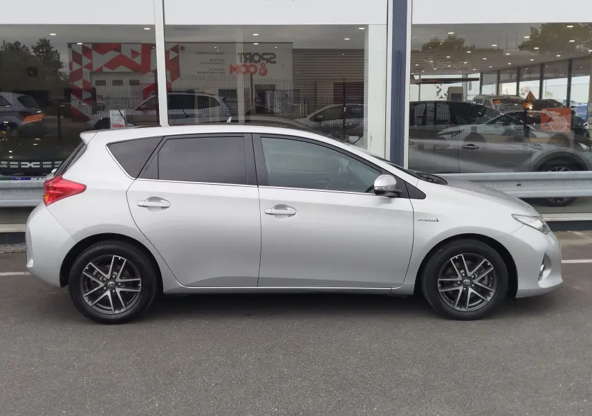 Profil droit d'une Toyota Auris gris aluminium de 2015, version hybride avec jantes alliage et vitres teintées.