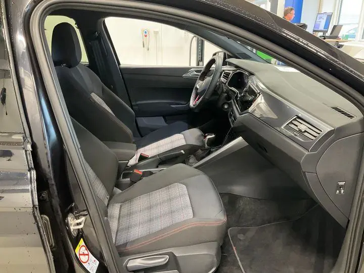 Vue intérieure côté conducteur de la Volkswagen Polo GTI 2024 noire, sièges sport avec tissu à motif écossais et volant sport.