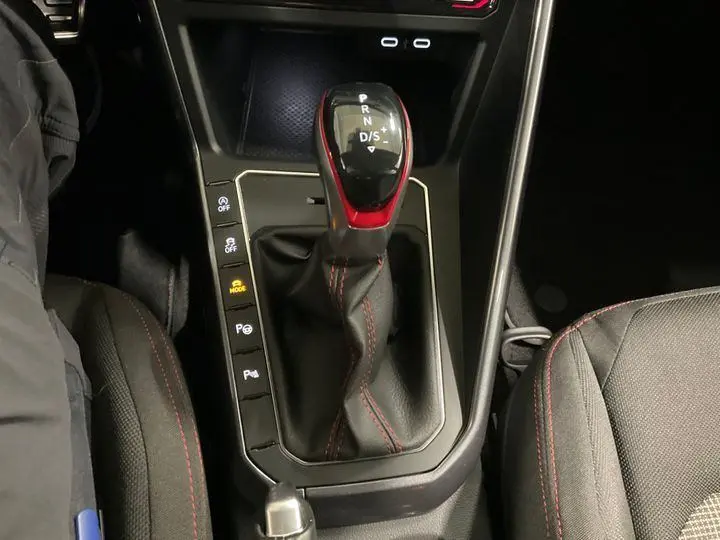 Vue rapprochée de la console centrale noire de la Volkswagen Polo GTI 2024 avec levier de vitesse automatique et surpiqûres rouges.