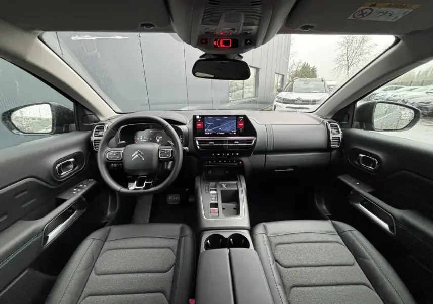 Vue intérieure avant du Citroën C5 Aircross 2025, tableau de bord et sièges tissu noir avec volant multifonction.