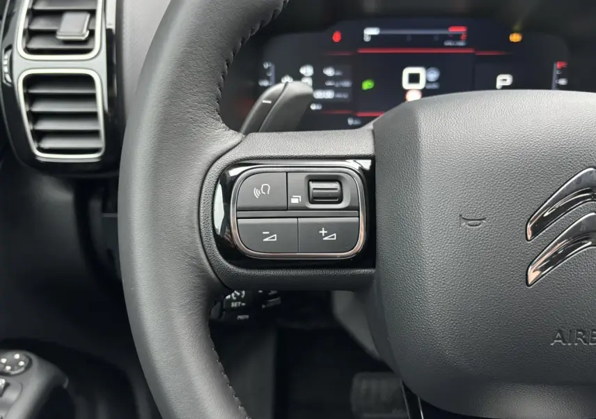 Gros plan sur le volant en cuir noir du Citroën C5 Aircross 2025 avec commandes intégrées et tableau de bord numérique flou.