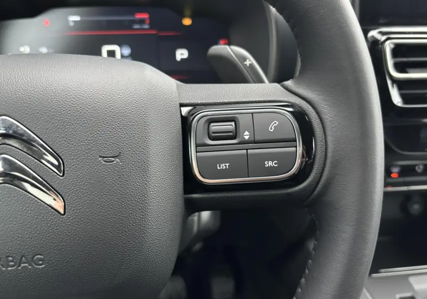 Gros plan sur le volant noir du Citroën C5 Aircross 2025, avec commandes intégrées côté droit et logo chromé central.