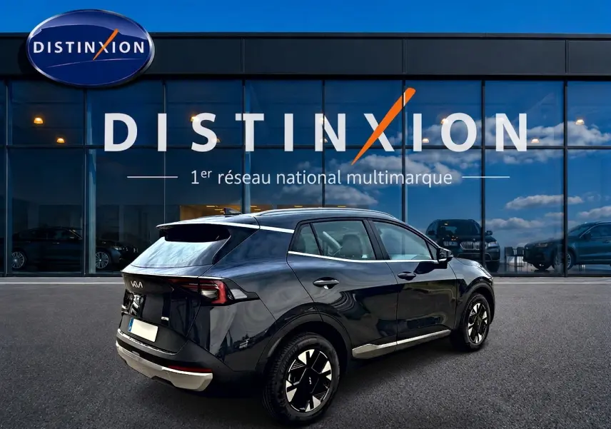Vue 3/4 arrière droite d’un KIA SPORTAGE gris eclipse 2026 garé devant une vitrine Distinxion.