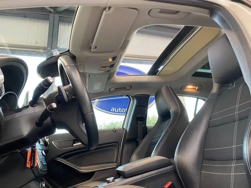 Intérieur du Mercedes GLA 200 Sensation 2017 vu côté conducteur, sièges cuir noirs avec surpiqûres blanches et toit ouvrant panoramique.