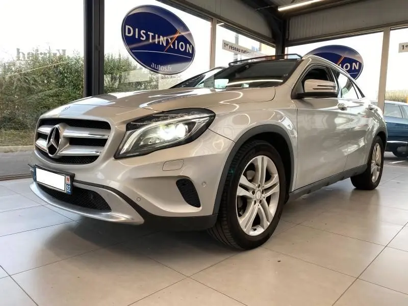 Mercedes GLA 200 Sensation gris montagne vu en 3/4 avant droit avec phares LED allumés dans un showroom.