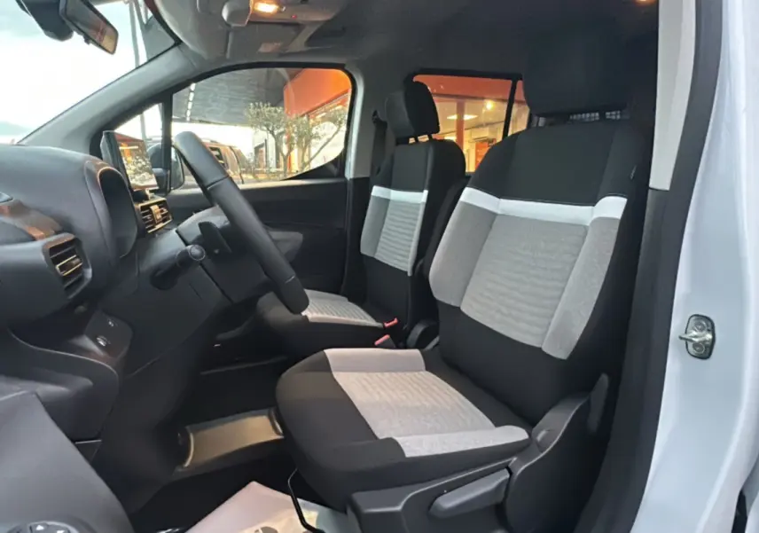 Vue intérieure côté gauche du poste de conduite du Citroën Berlingo 2026 avec sièges tissu bicolores gris et noir.