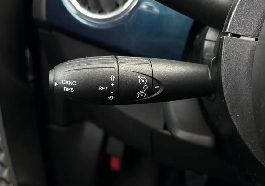 Gros plan sur la commande de régulateur de vitesse à gauche du volant dans l’habitacle bleu du Fiat 500 Hybrid 2024.