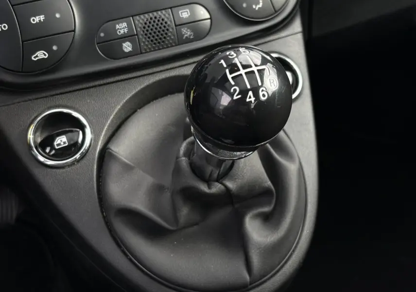 Gros plan sur le levier de vitesses manuel noir dans l’habitacle de la Fiat 500 Hybrid 2024, avec commandes proches.