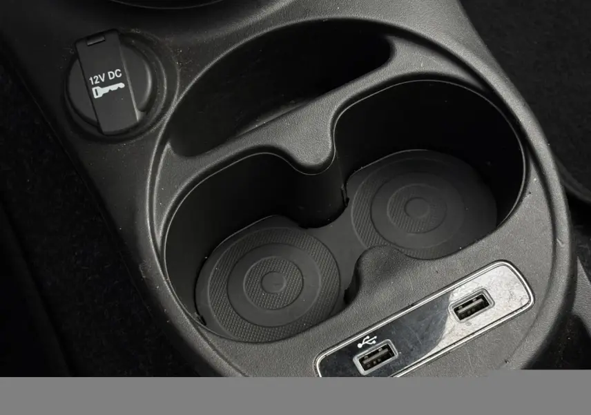 Gros plan sur la console centrale noire du Fiat 500 Hybrid 2024, avec porte-gobelets, prise 12V et ports USB visibles.
