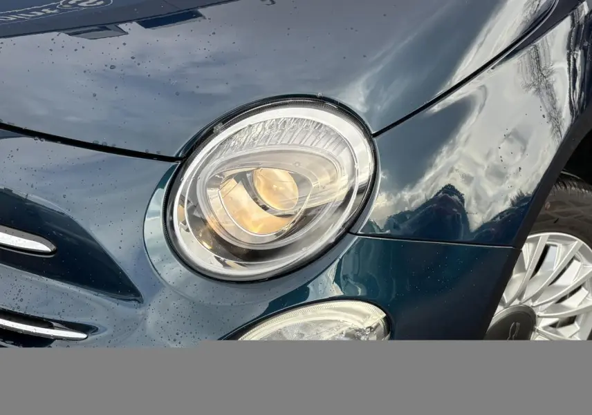 Gros plan sur le phare avant gauche d'une FIAT 500 Hybrid 70 bleu Dipinto avec jante alliage 15 pouces visible.
