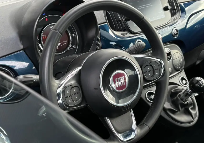 Vue intérieure centrée sur le volant noir et la console bleu Dipinto avec levier de vitesses manuel de la Fiat 500 Hybrid 2024.