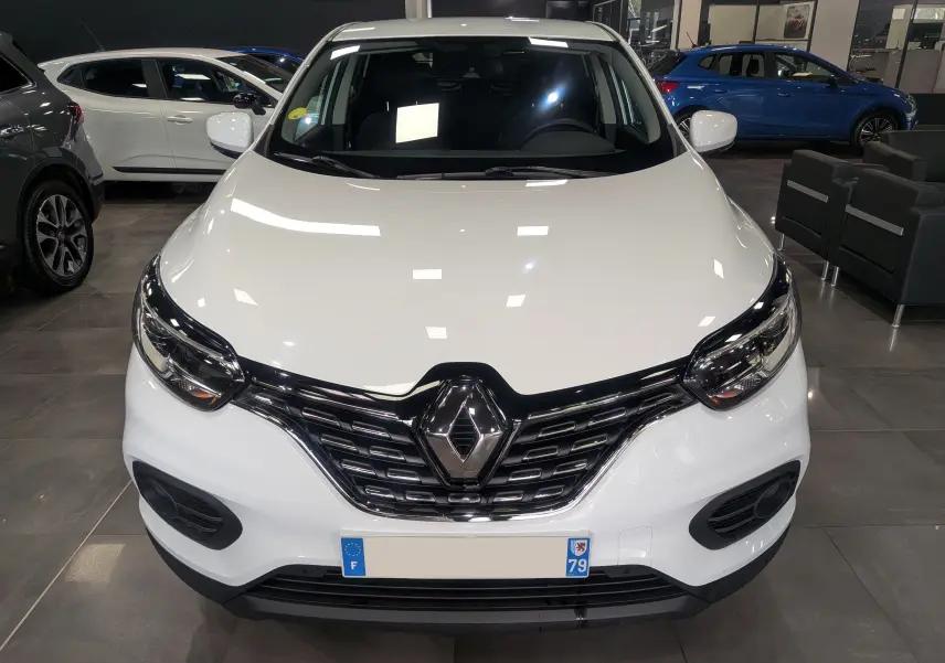 Vue avant d'un Renault Kadjar blanc Glacier 2021 en showroom, mettant en valeur sa calandre noire et ses phares LED.