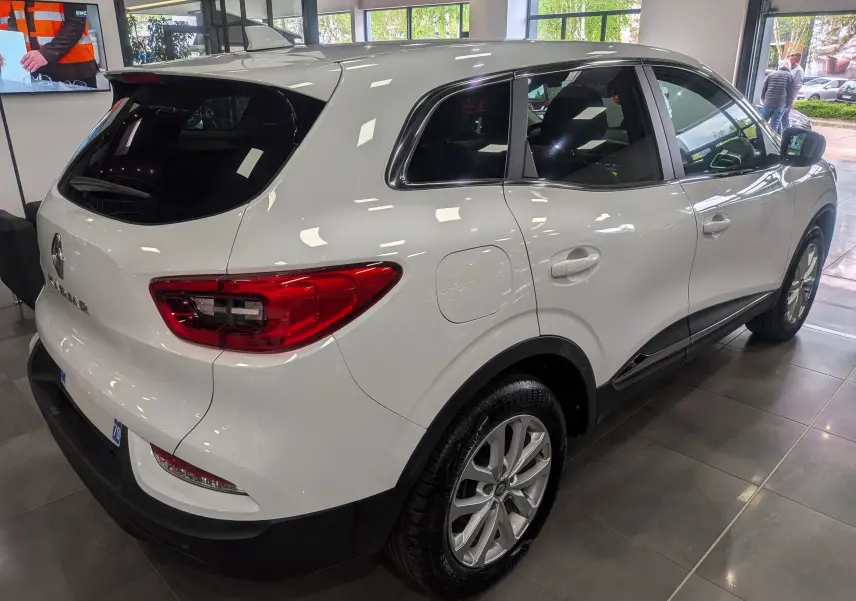 Vue 3/4 arrière droite d'un Renault Kadjar blanc Glacier 2021 en showroom, avec feux arrière rouges et jantes alliage.