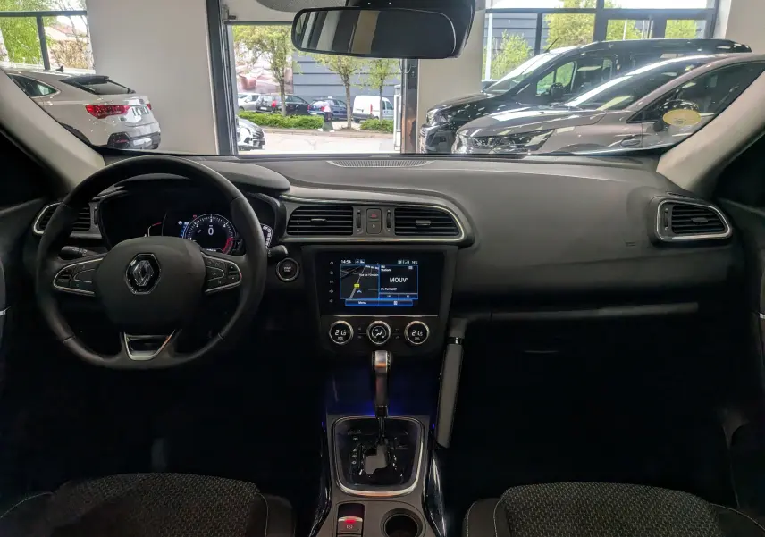 Vue intérieure frontale du tableau de bord du Renault Kadjar blanc, avec volant multifonction et écran tactile central allumé.