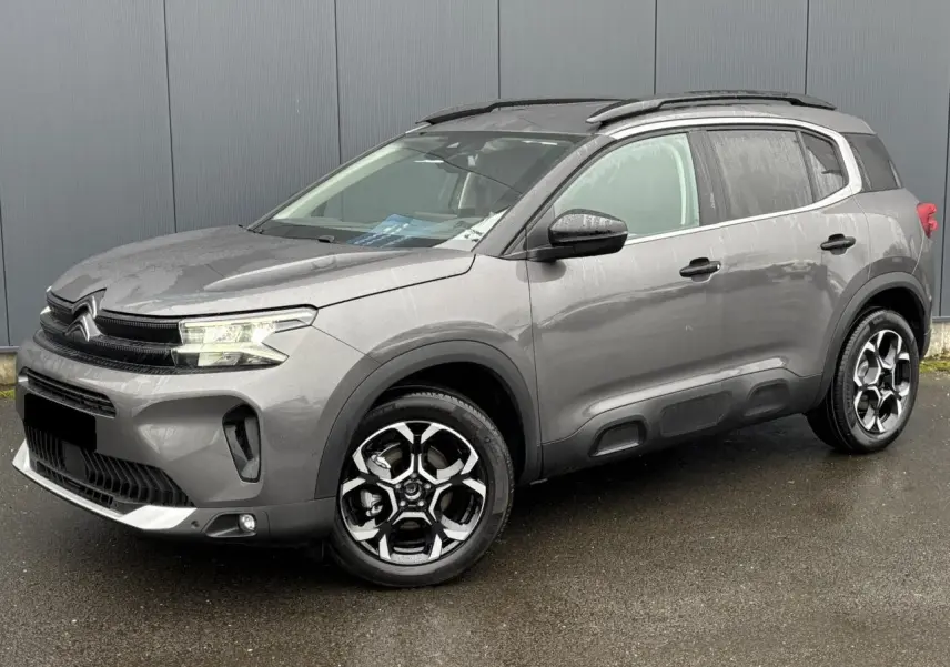 Vue 3/4 avant droite d’un Citroën C5 Aircross gris Platinium avec jantes alliage bi-ton et barres de toit noires.