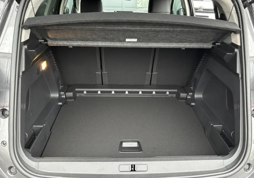 Coffre ouvert vu de l'arrière du Citroën C5 Aircross gris Platinium avec cache-bagages relevé et intérieur noir.