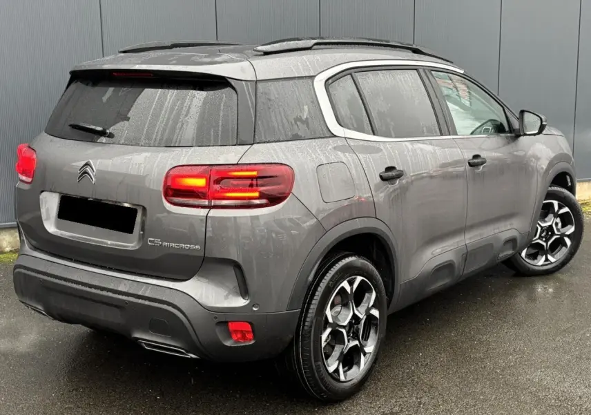 Vue 3/4 arrière droite du Citroën C5 Aircross gris Platinium avec feux arrière allumés et jantes alliage bi-ton.