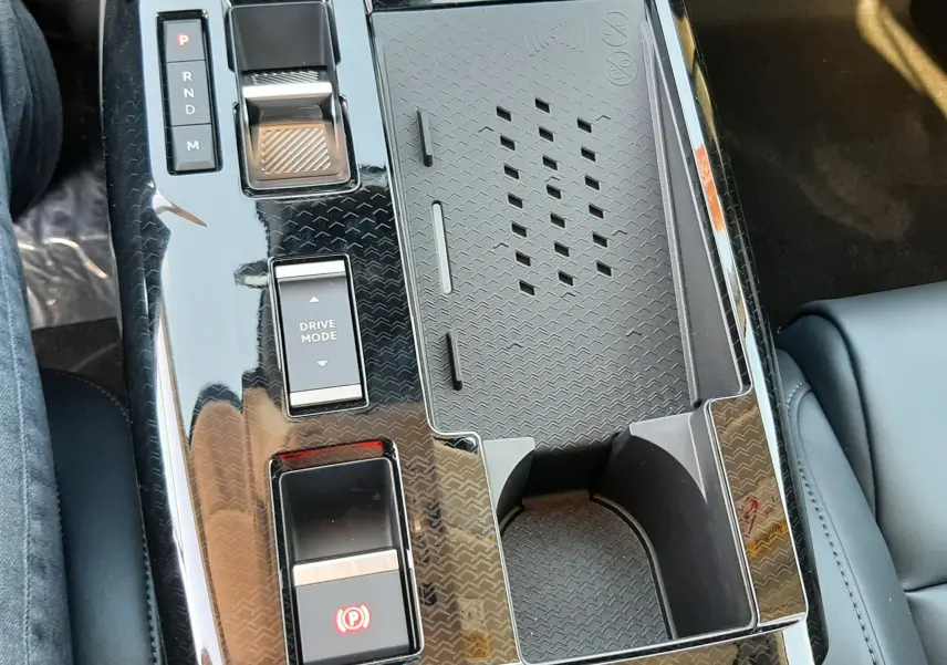 Vue rapprochée de la console centrale noire brillante du Citroën C5 Aircross hybride 2026 avec commandes de boîte auto et porte-gobelet.