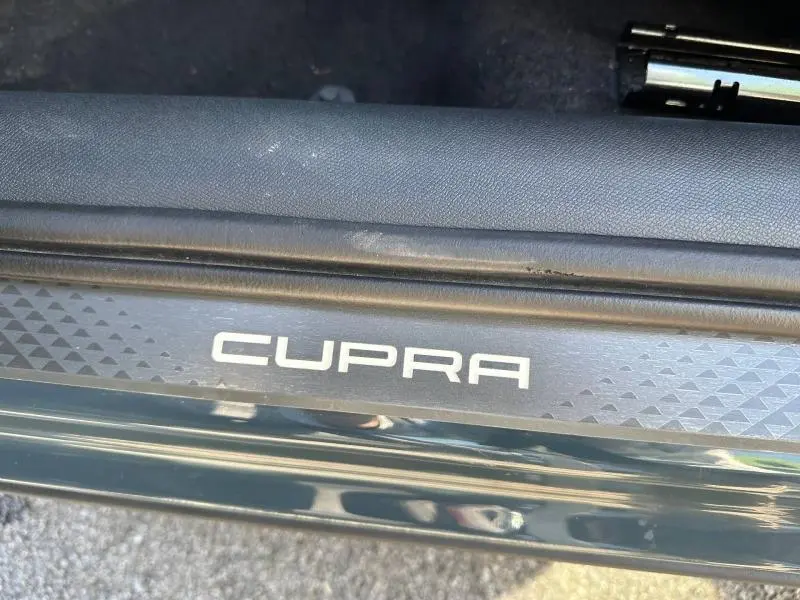 Gros plan sur la plaque de seuil de porte avec logo CUPRA sur fond noir texturé, intérieur d’une Formentor bleu.