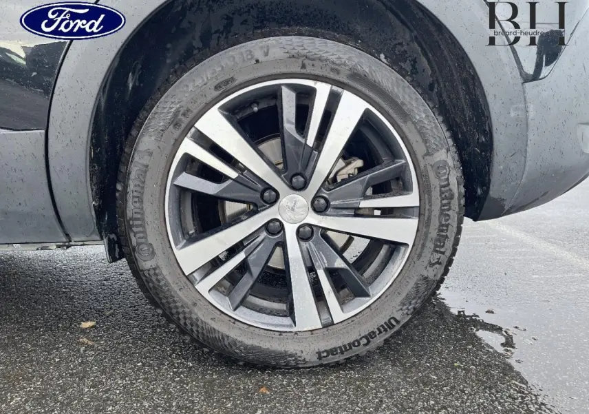 Gros plan sur la roue avant gauche d’un Peugeot 5008 noir Perla Nera avec jante alliage bicolore.