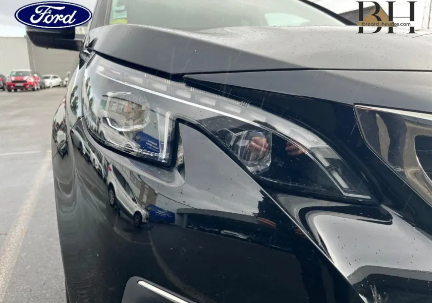 Gros plan sur le phare avant droit noir Perla Nera du Peugeot 5008 avec reflets et pluie sur la carrosserie.