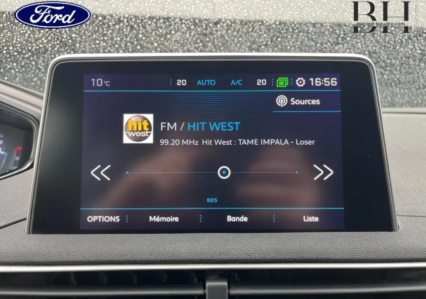 Écran tactile central d'infodivertissement Peugeot 5008 noir, affichant la radio FM Hit West à 16h56 par temps pluvieux.