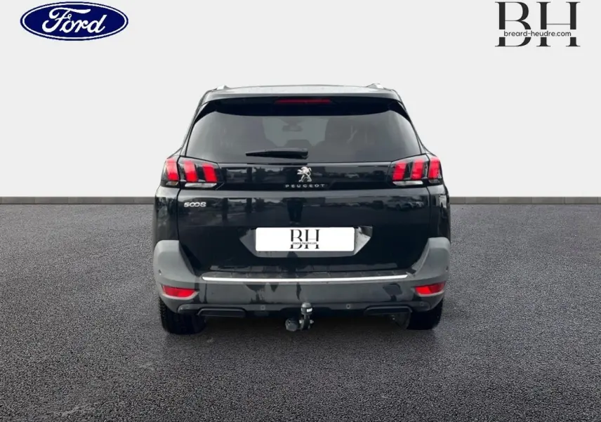 Vue arrière d'un Peugeot 5008 noir Perla Nera avec hayon, feux LED et attelage visible sur sol goudronné.