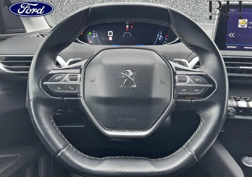 Vue rapprochée du volant cuir noir multifonction d'un Peugeot 5008 avec tableau de bord numérique et écran tactile à droite.