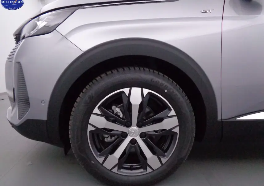 Gros plan sur la roue avant gauche et la carrosserie gris artense métal du Peugeot 3008 GT 2023, soulignant la jante bicolore et le badge GT.