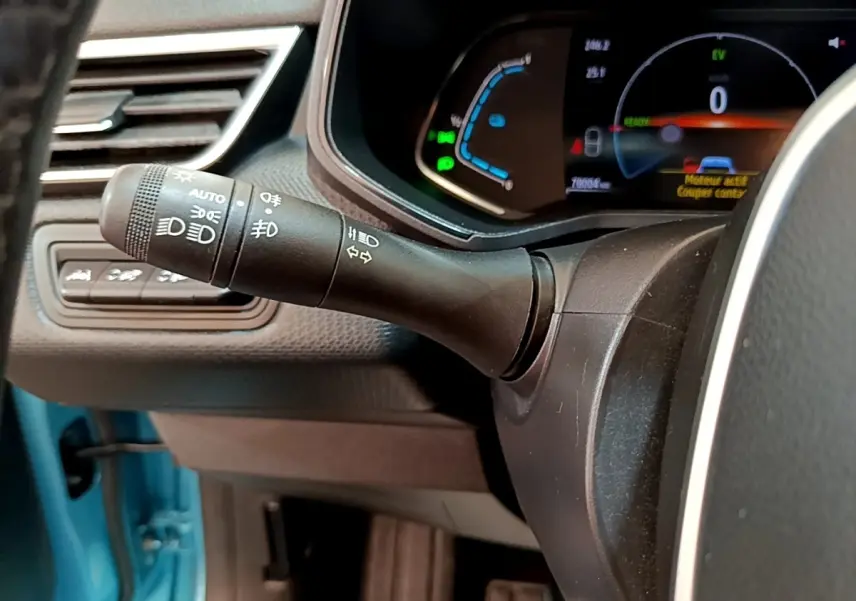 Gros plan sur la commande des phares et clignotants à gauche du volant dans l’habitacle bleu d’une Renault Clio hybride.