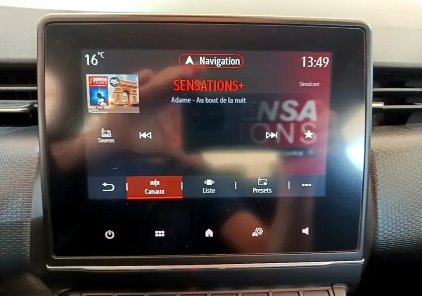 Écran tactile central de la Renault Clio Business E-Tech hybride bleu, affichant la radio Sensations+ en mode navigation.