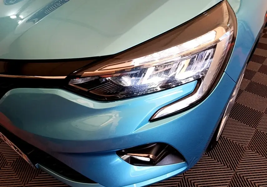 Gros plan sur le phare avant droit d'une Renault Clio Business E-Tech hybride 2021 bleu métallisé, avec feux LED allumés.