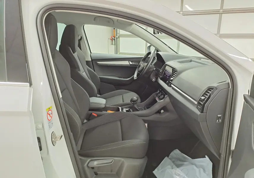 Vue intérieure côté gauche du Skoda Karoq blanc Lune 2025, sièges tissu noirs et tableau de bord moderne.
