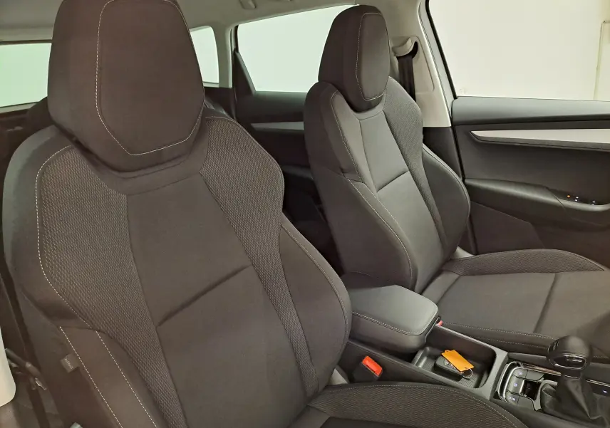 Vue intérieure des sièges avant en tissu noir du Skoda Karoq 1.5 TSI 150 DSG7, avec console centrale et levier de vitesse.
