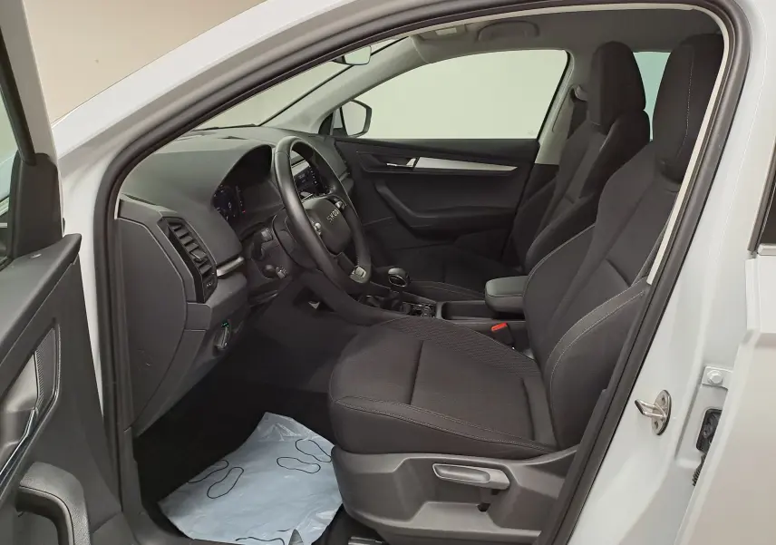 Vue intérieure côté conducteur du Skoda Karoq blanc Lune 2025, sièges noirs et tableau de bord moderne.