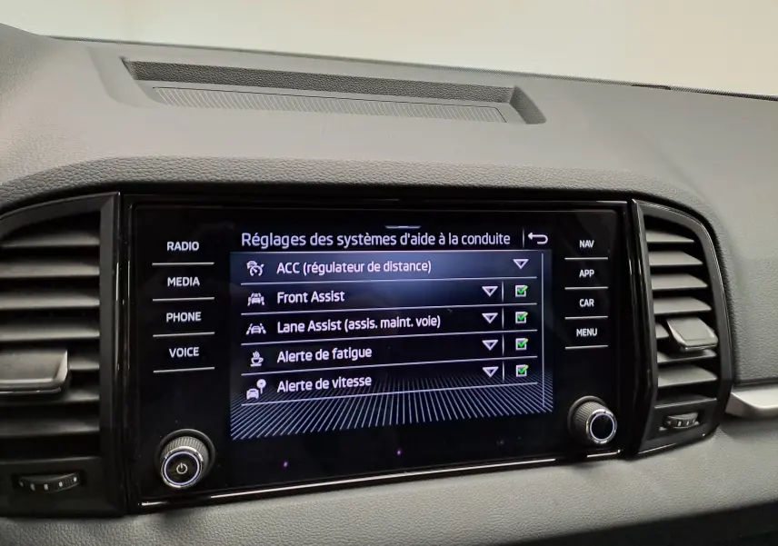 Écran central du tableau de bord du Skoda Karoq blanc Lune, affichant les réglages des aides à la conduite.