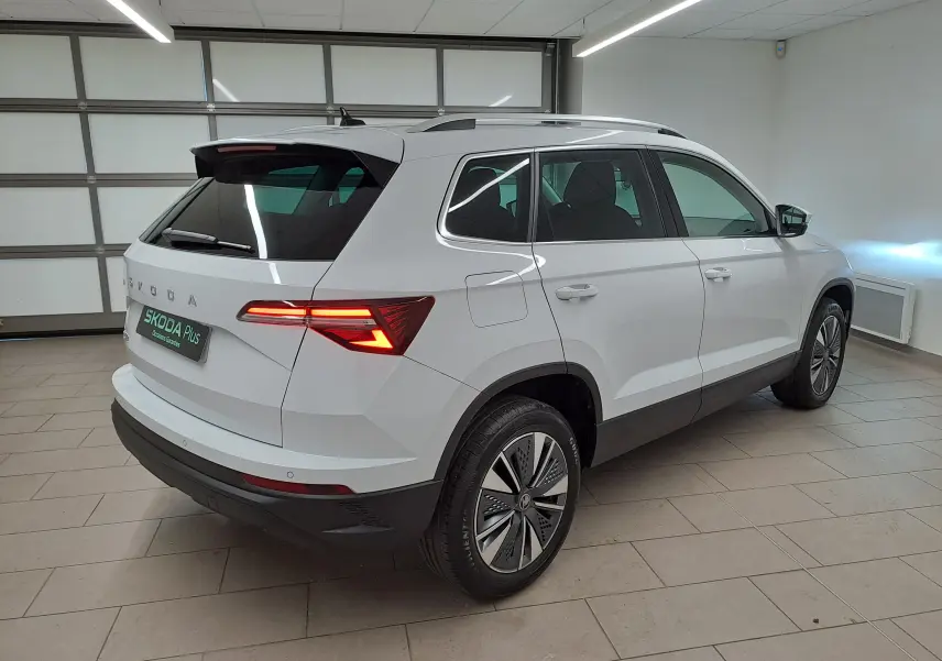 Vue 3/4 arrière droite du Skoda Karoq blanc Lune, avec feux arrière allumés et détails chromés autour des vitres.
