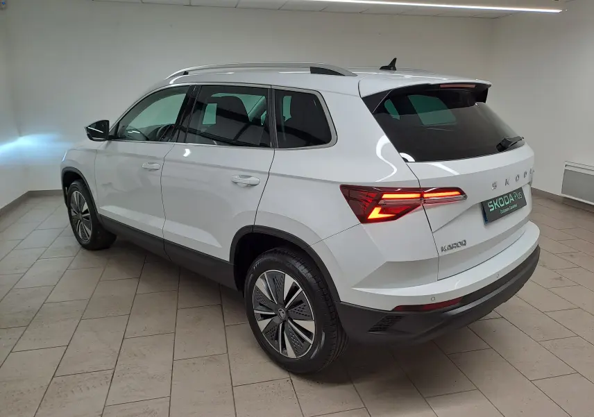 Vue 3/4 arrière droite du Skoda Karoq blanc Lune avec feux allumés et pack chrome extérieur visible.