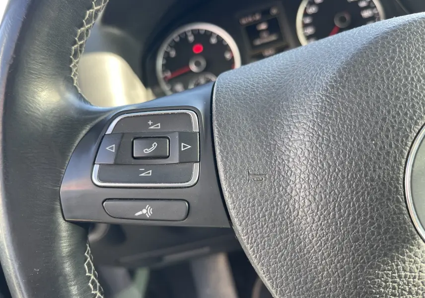 Gros plan sur les commandes au volant à gauche du Volkswagen Tiguan gris foncé, tableau de bord en arrière-plan flou.