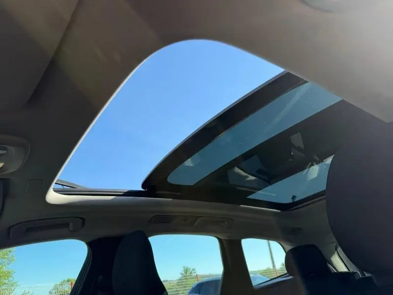 Vue intérieure du toit panoramique en verre du Volvo XC60 gris 2024, avec ciel bleu visible à travers l'ouverture.