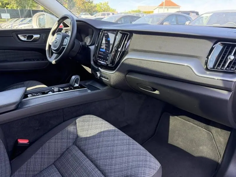Vue intérieure côté conducteur du Volvo XC60 T6 hybride rechargeable 2024, montrant tableau de bord moderne et sièges tissu gris.
