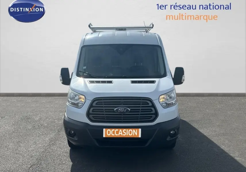 Vue de face du Ford Transit Fourgon blanc de 2015 avec calandre noire et phares allumés.