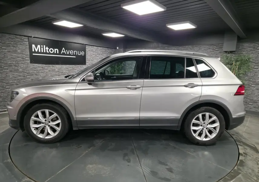 Volkswagen Tiguan gris métallisé vu de profil côté gauche dans un showroom avec jantes alliage 18 pouces.
