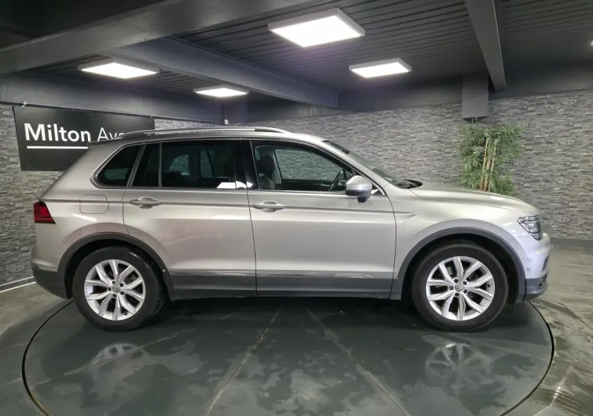 Profil droit d'un Volkswagen Tiguan gris métallisé 2020 avec jantes alliage 18 pouces dans un showroom intérieur.