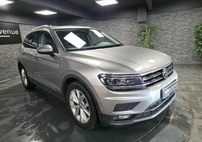 Volkswagen Tiguan gris métallisé vu en 3/4 avant droit dans un showroom avec jantes alliage 18 pouces.