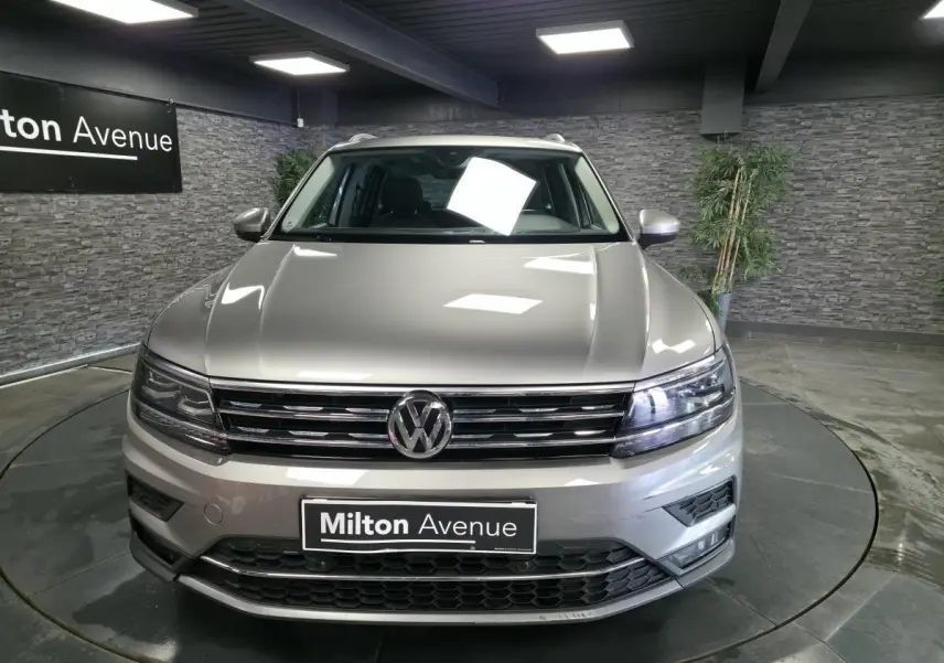 Vue frontale d'un Volkswagen Tiguan gris métallisé 2020 avec calandre chromée et phares LED allumés en showroom.