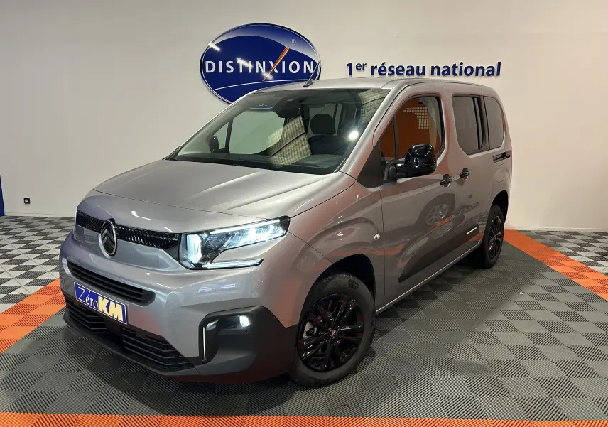 Citroën Berlingo Multispace gris Artense en 3/4 avant droit avec jantes noires et feux allumés en intérieur showroom.