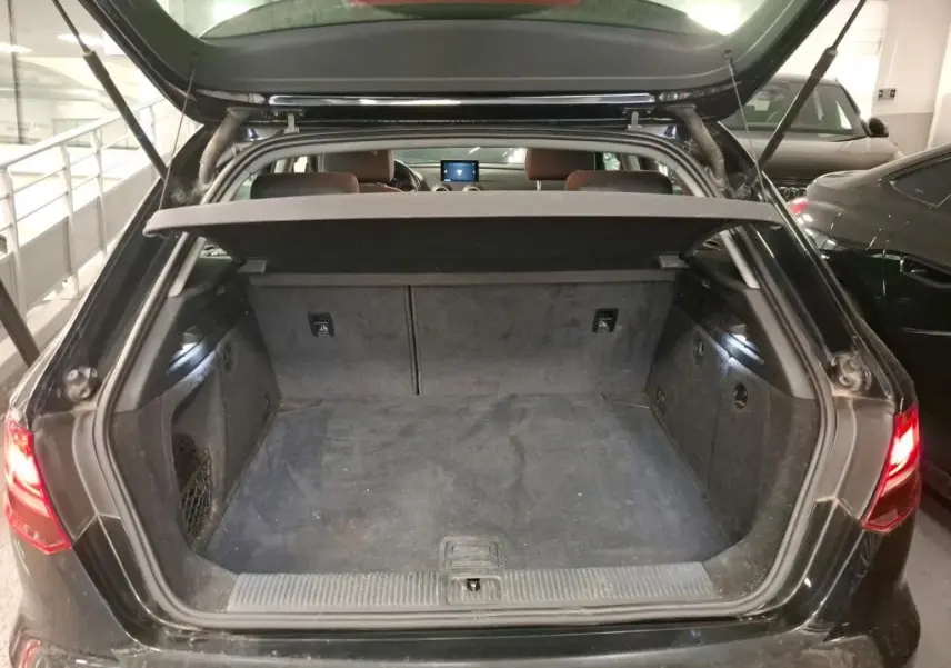 Coffre ouvert vu de l'arrière d'une Audi A3 Sportback noire, montrant l'espace de chargement vide et la plage arrière.