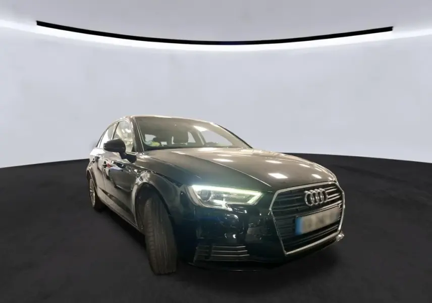 Audi A3 Sportback noir vue 3/4 avant gauche avec phares allumés sur fond neutre intérieur.