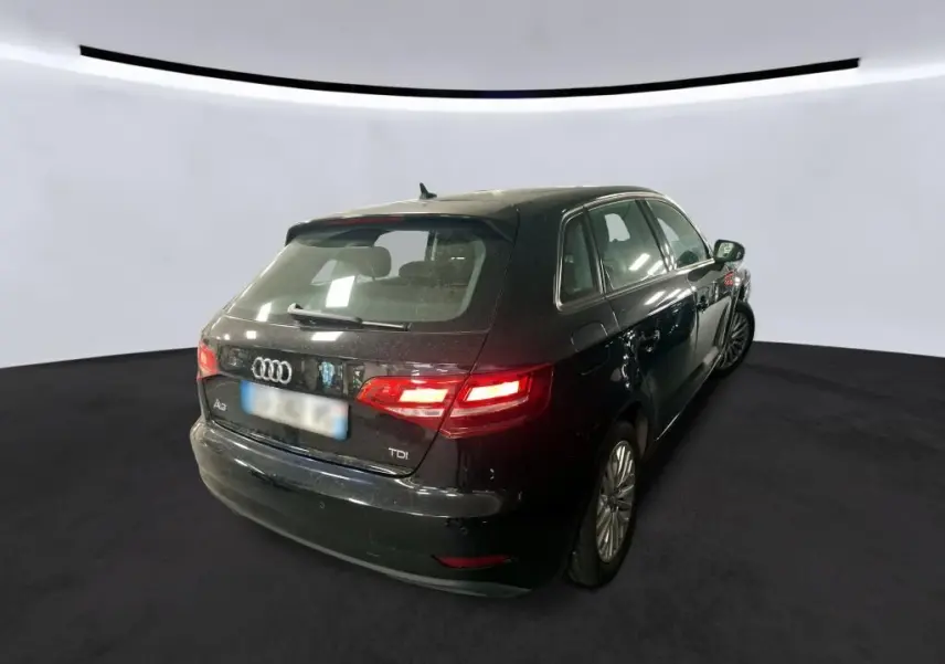 Audi A3 Sportback noire vue 3/4 arrière droit, feux arrière allumés dans un studio lumineux.